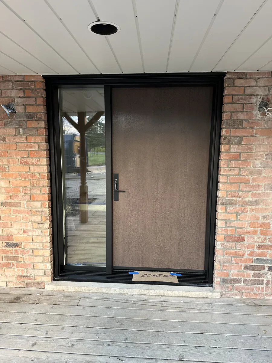 Walnut-finish entry door with black frame and full sidelite in the estate's brick