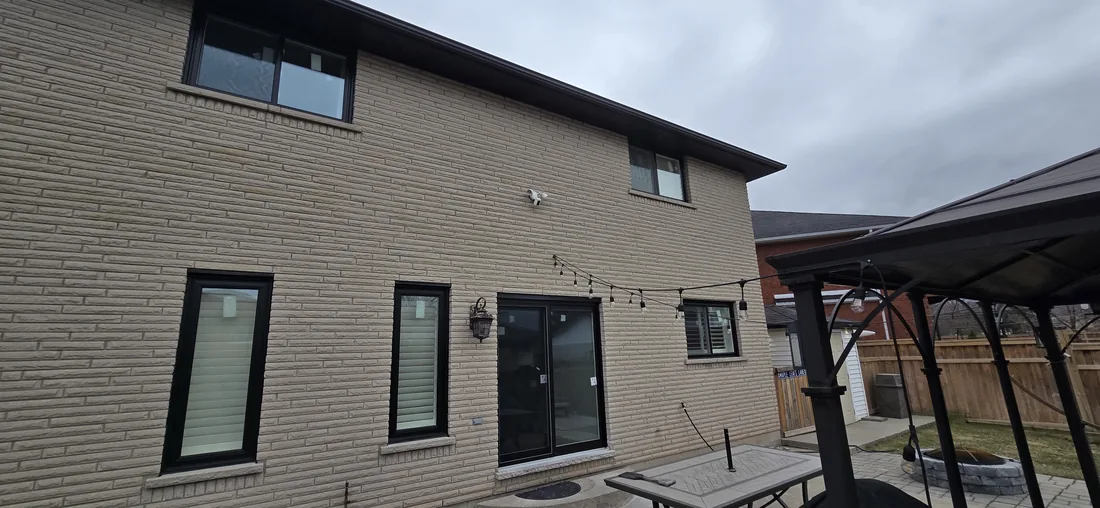 Rear of the Stoney Creek home with new black windows and sliding patio door in stone brick