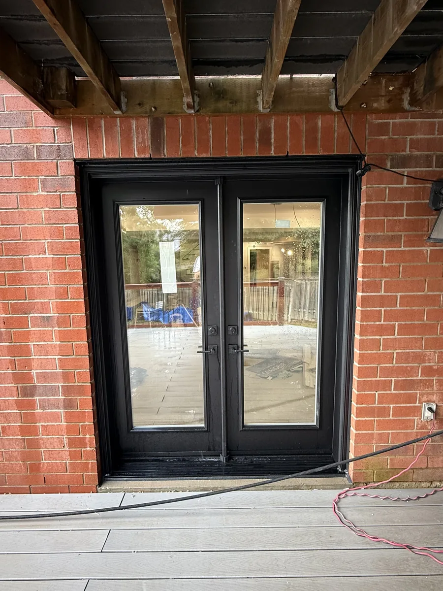 New black garden doors installed in the red brick wall beneath the deck of the Newmarket home