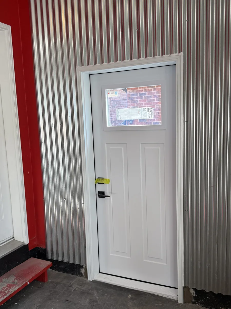 New white door installed in a corrugated steel feature wall inside the workshop space