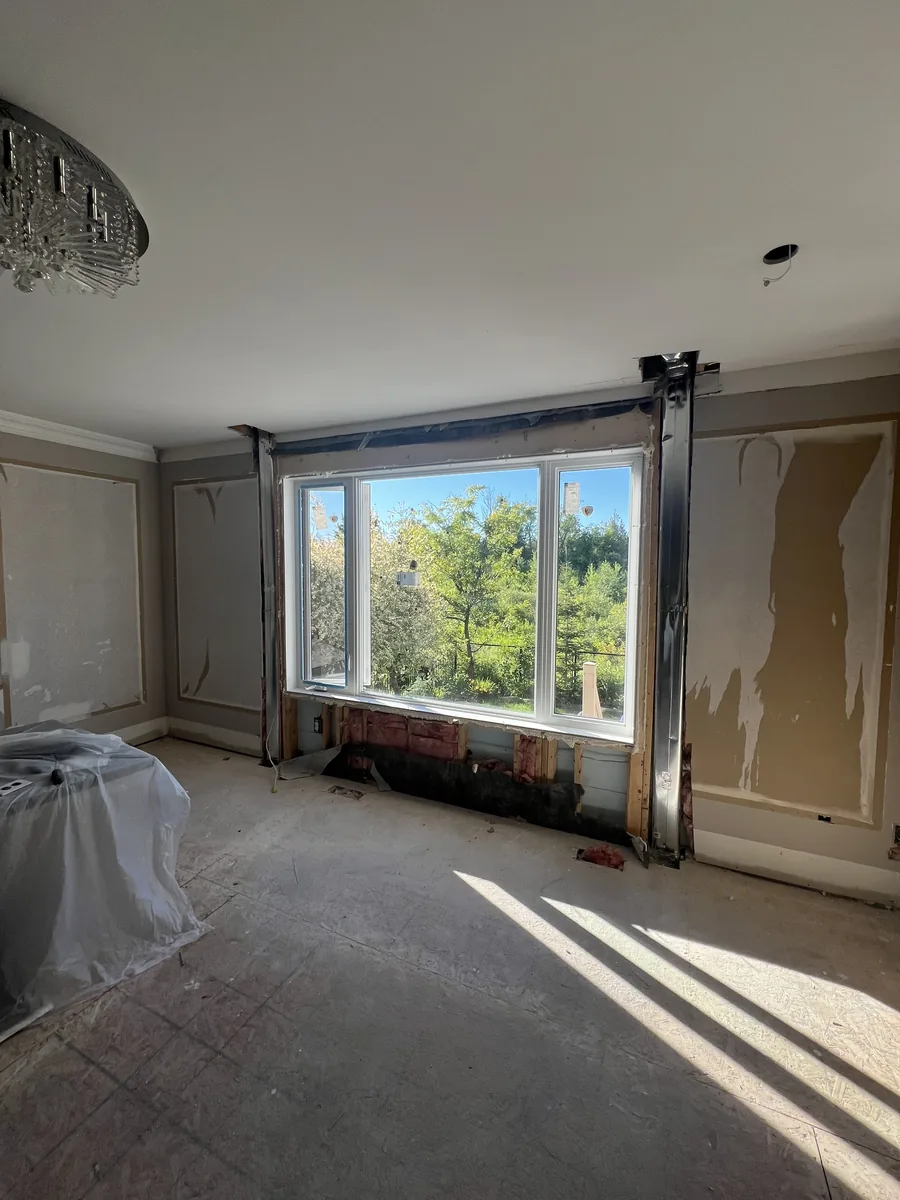 The new nine-foot living room window installed with the wall being rebuilt around it, greenbelt visible outside